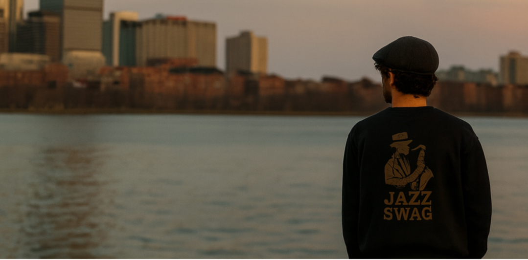 Person wearing a black sweatshirt with 'Jazz Swag' design, standing by a waterfront with city skyline in the background.
